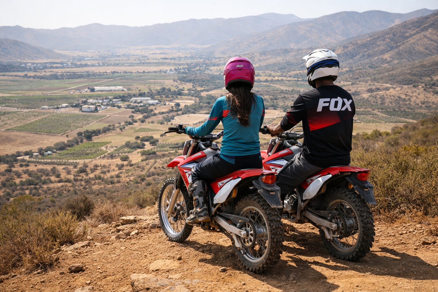 Two dirt bike riders overlooking Valle de Guadalupe vineyard valley from a hilltop trail